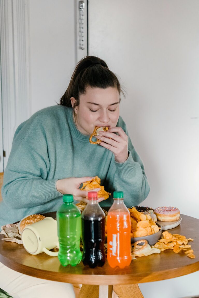 Young woman enjoys assorted fast food and snacks indoors with a variety of sodas.